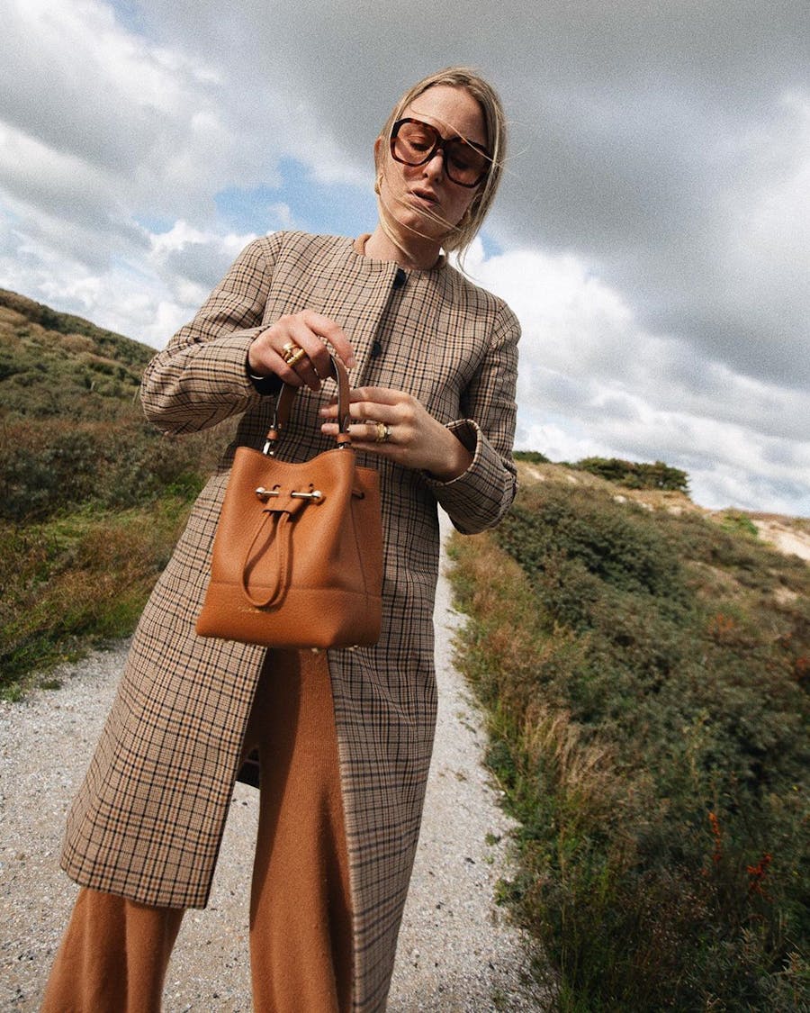 A woman holding a brown purse on top of a dirt road