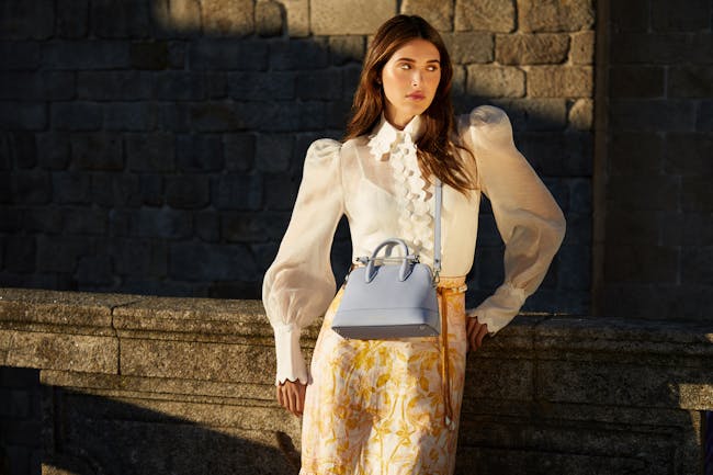 A woman standing next to a stone wall holding a purse