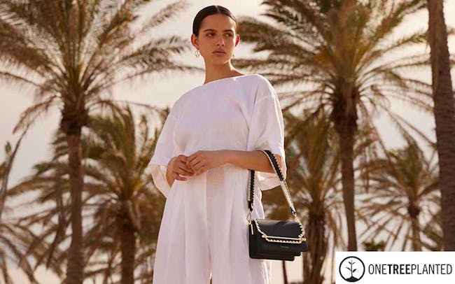 A woman standing on a beach holding a black purse