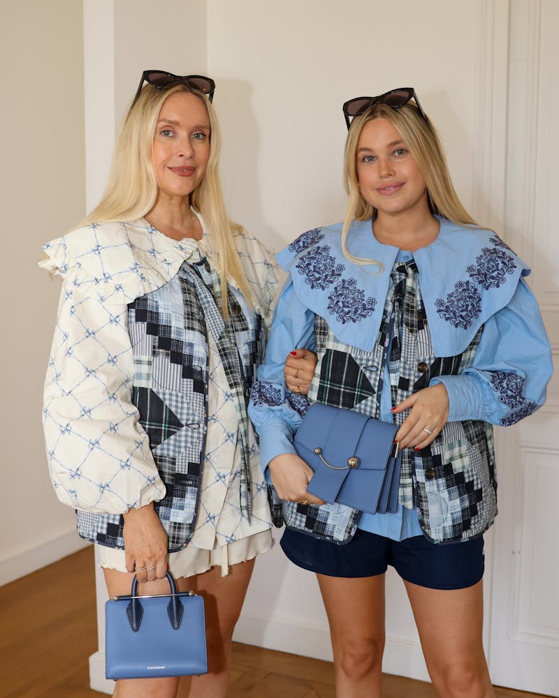 Two women standing next to each other holding purses