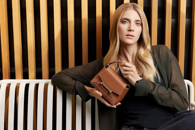 A woman sitting on a white bench holding a brown purse