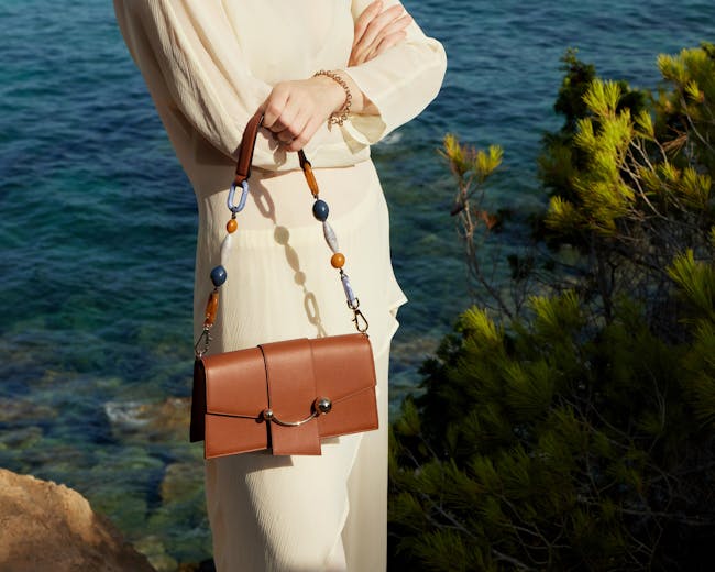 A woman is holding a brown purse by the water
