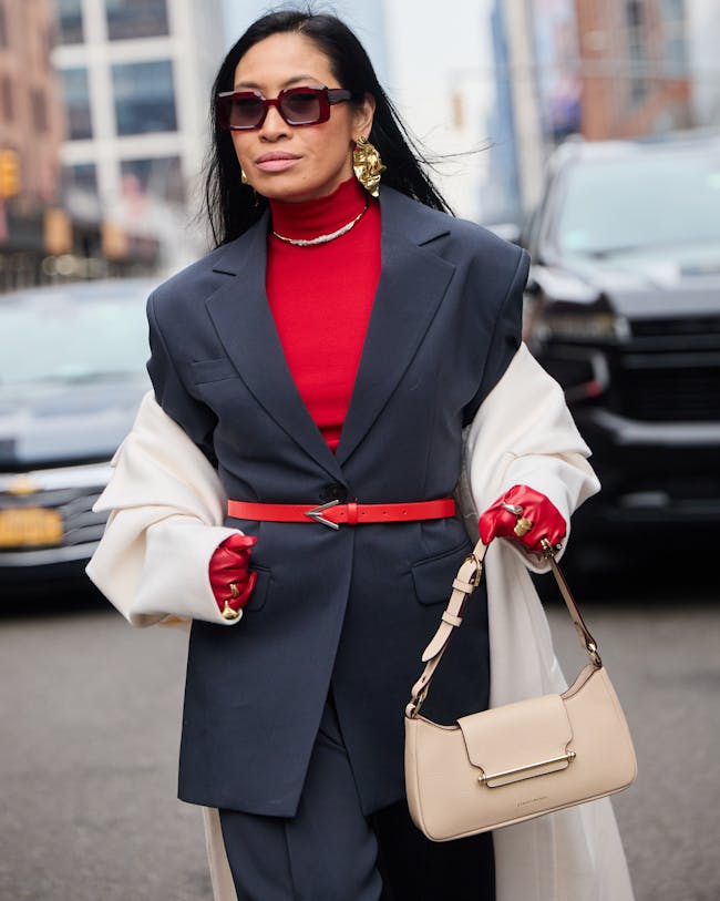A woman in a red shirt and black suit carrying a beige purse