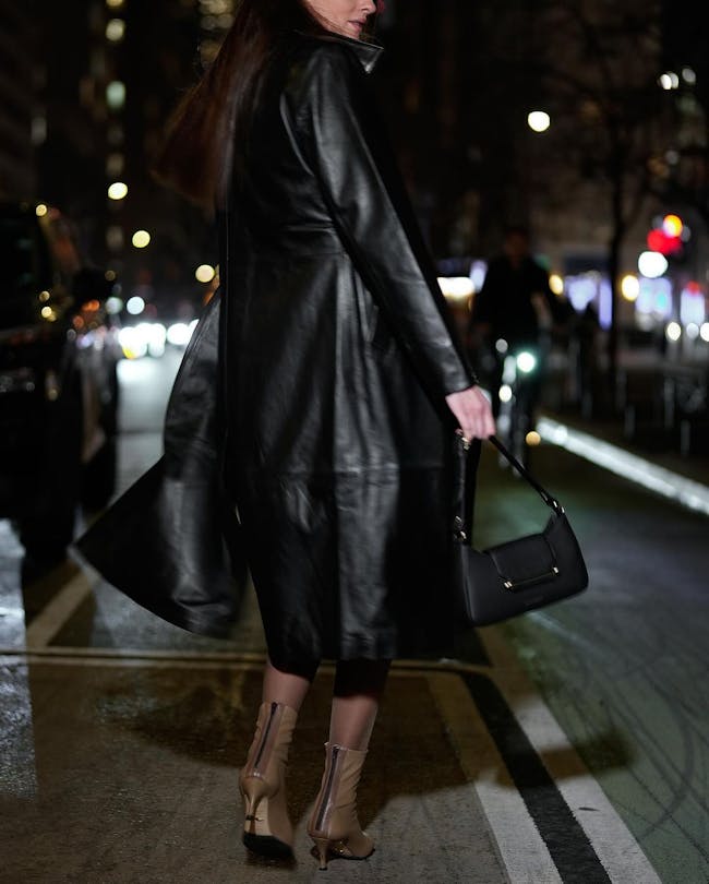 A woman in a black leather coat is crossing the street