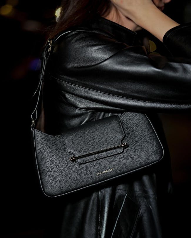 A woman in a black leather jacket holding a black purse