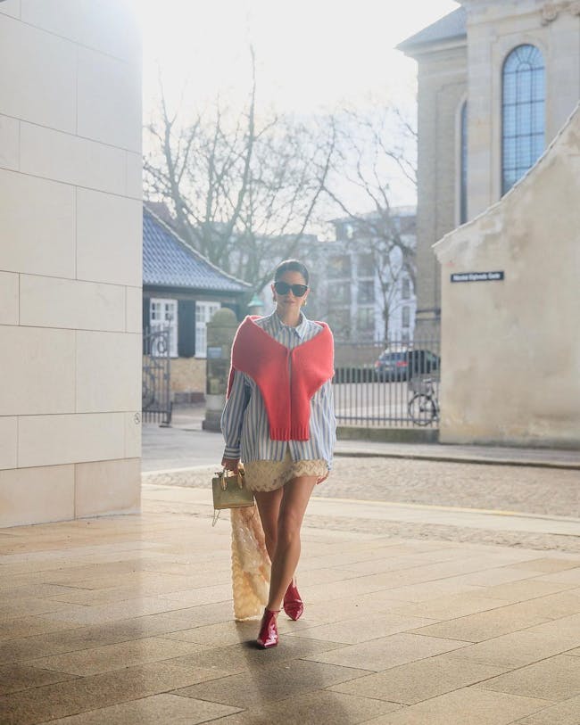 A woman walking down a sidewalk carrying a bag