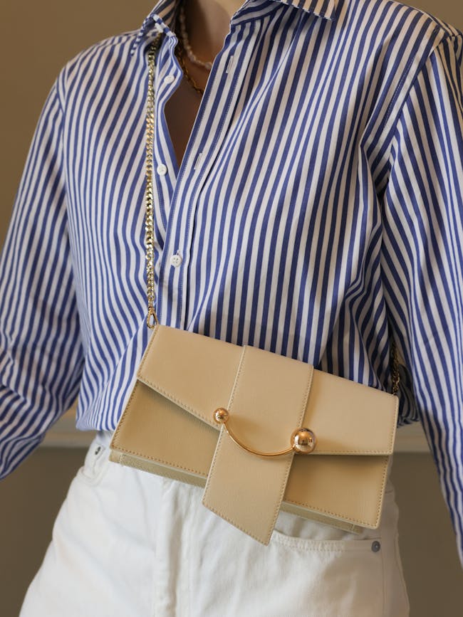 A woman wearing a blue and white striped shirt holding a tan purse