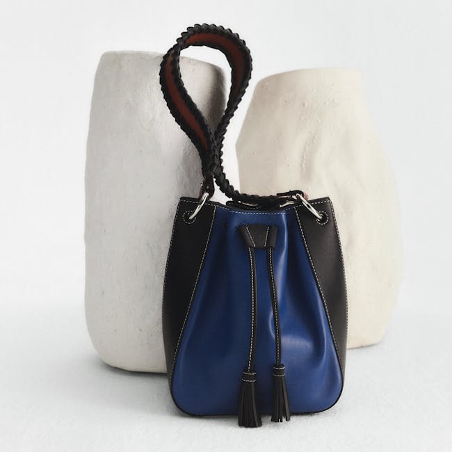 A black and blue purse sitting next to a white vase