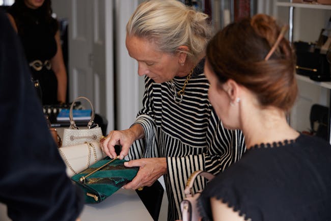 A woman looking at a purse while another woman looks on