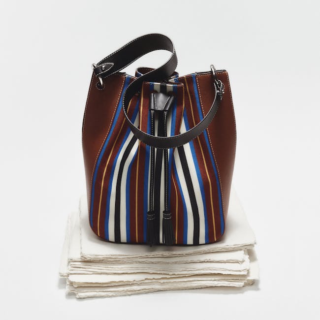 A brown and blue striped purse sitting on top of a stack of white napkins