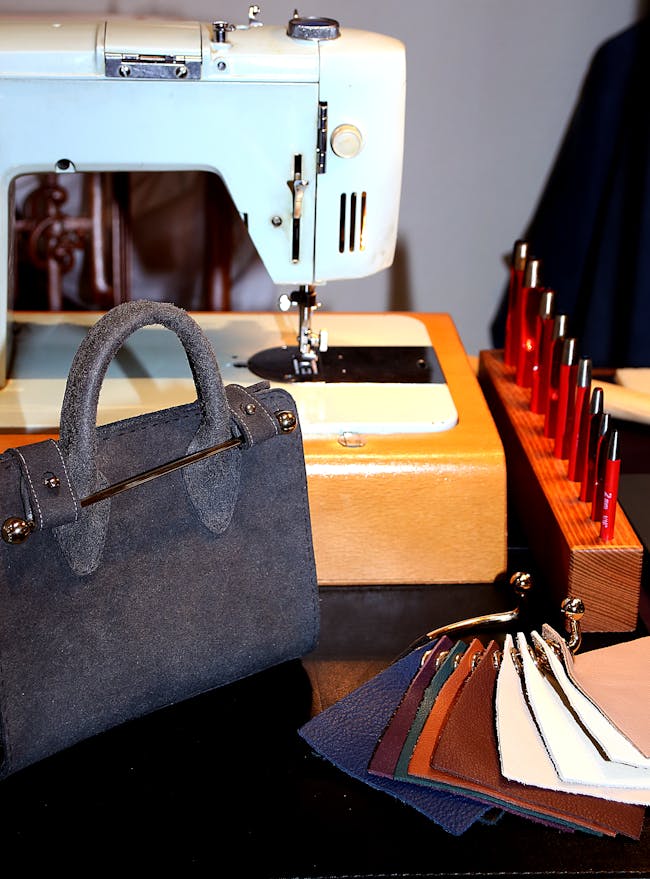 A detailed shot of our Strathberry nano tote in suede navy, along with leather swatch samples from our collection, and stitching machine for customisation, as displayed at an event in Edinburgh.