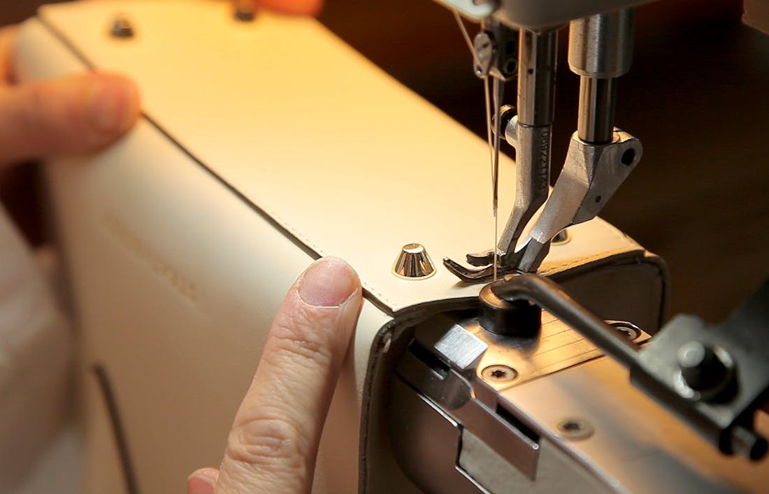 A detailed shot of the construction of a Strathberry handbag. Focusing on the gold hardware feet on the base of the handbag and the detailed stitching around the edge of the base of the handbag. Shown in the atelier in Ubrique, Spain.