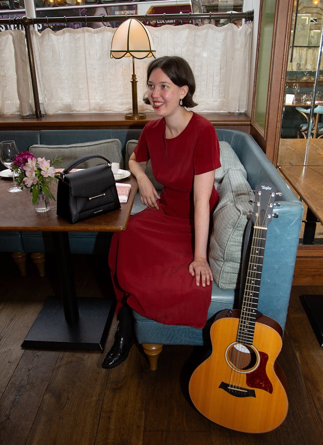A woman in a red dress sitting at a table with a guitar