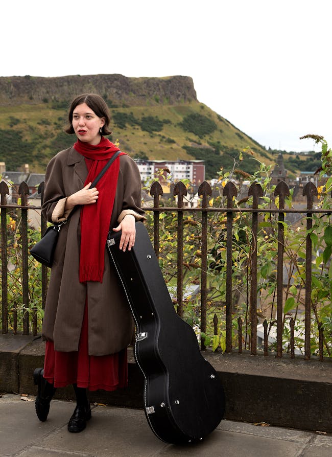A woman standing next to a fence holding a guitar case