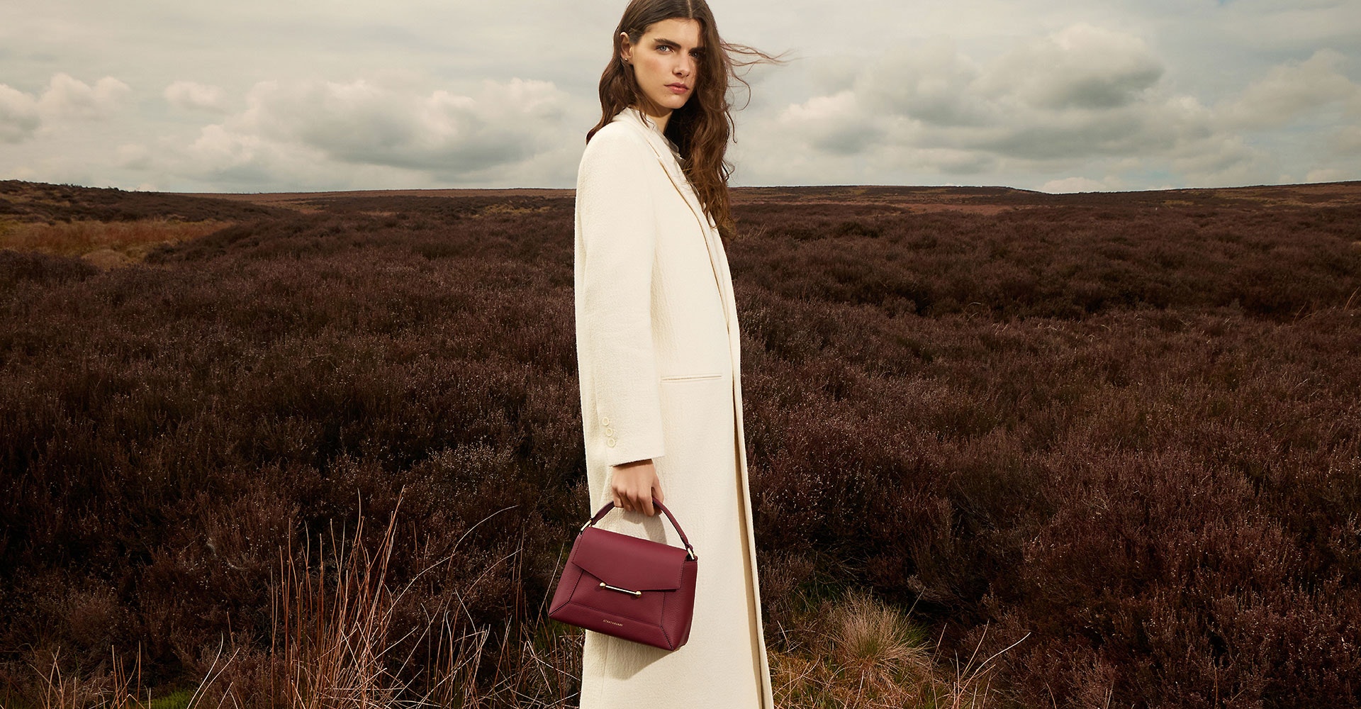 A woman standing in a field holding a red purse