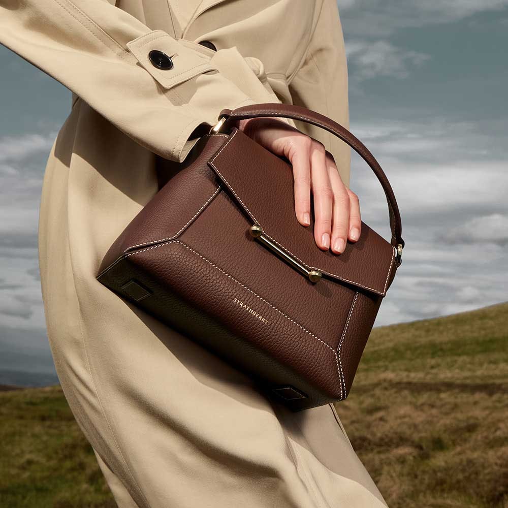 A woman in a trench coat carrying a brown purse