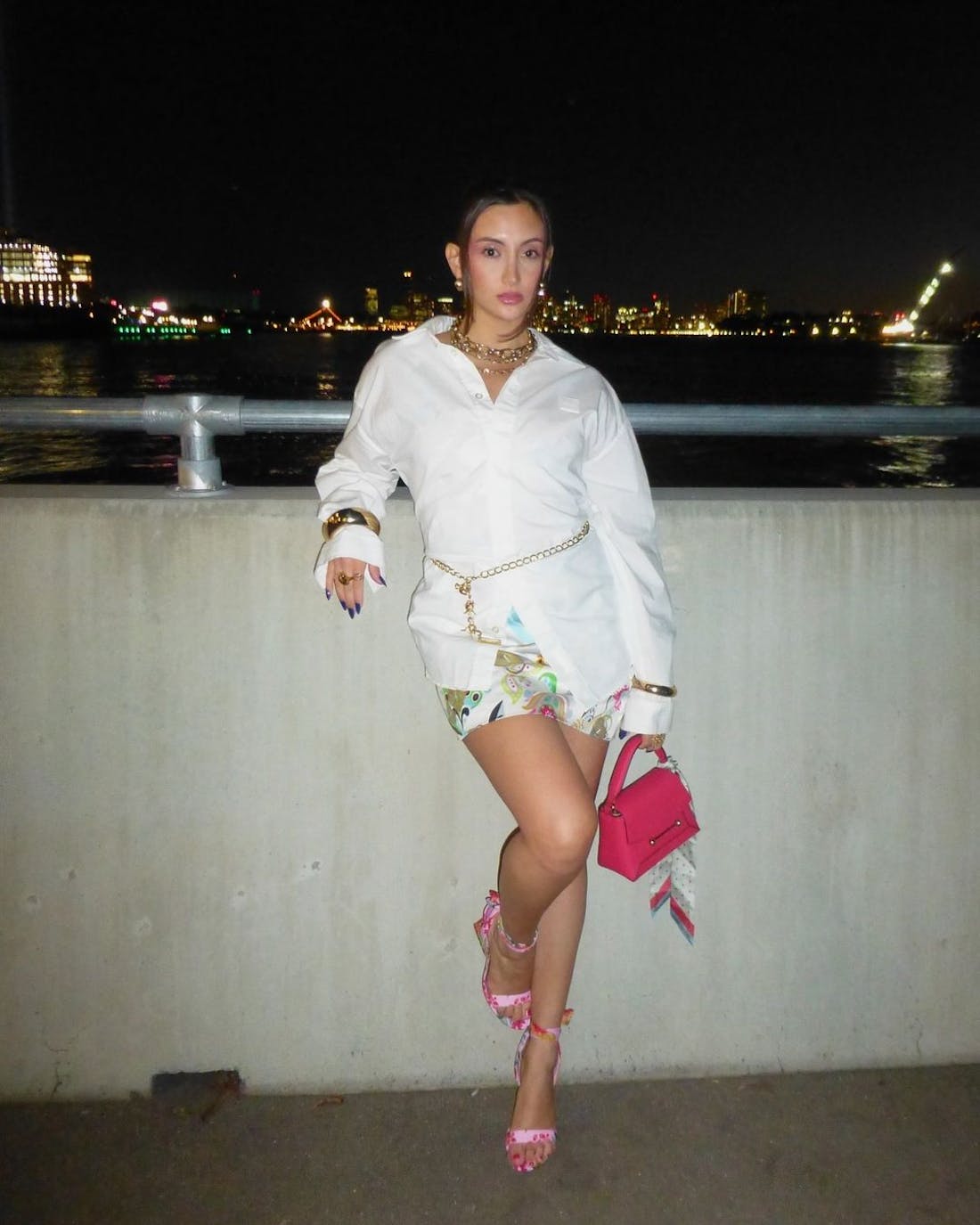 A woman in a white dress and pink purse leaning against a wall