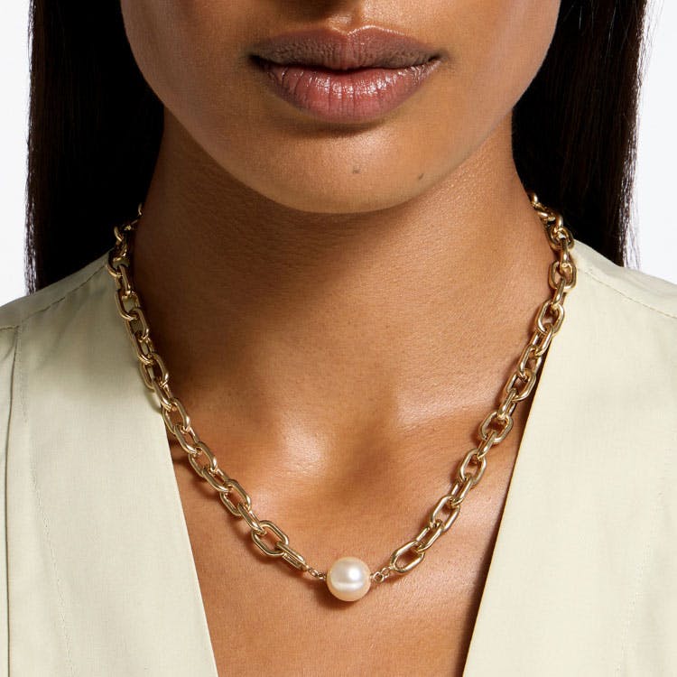 A close up of a person wearing a gold chain necklace with a pearl