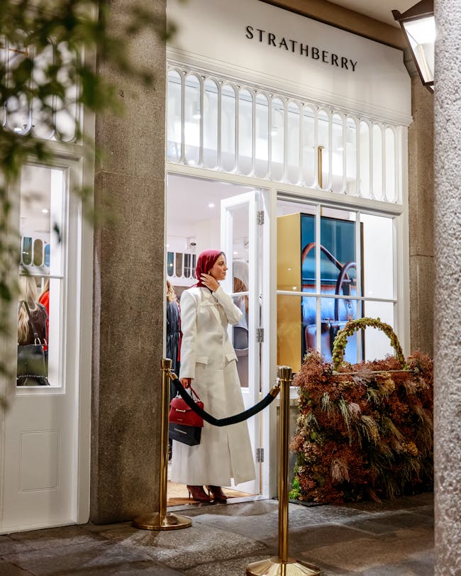 A woman in a white coat is standing outside of a store