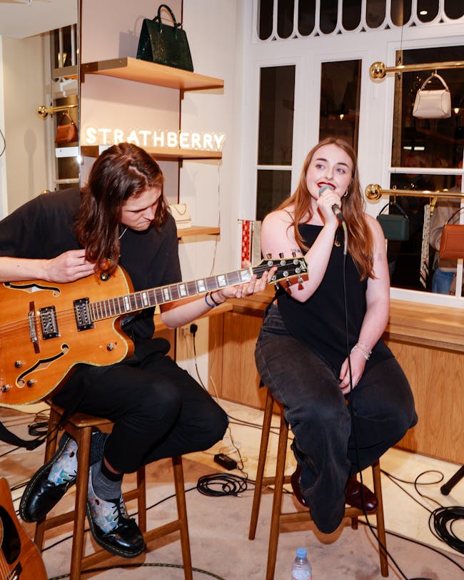 A woman sitting on a stool next to a man holding a guitar