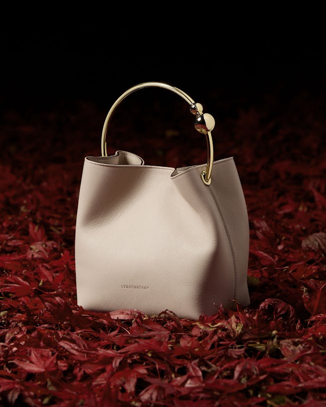 A white purse sitting on top of a pile of red leaves