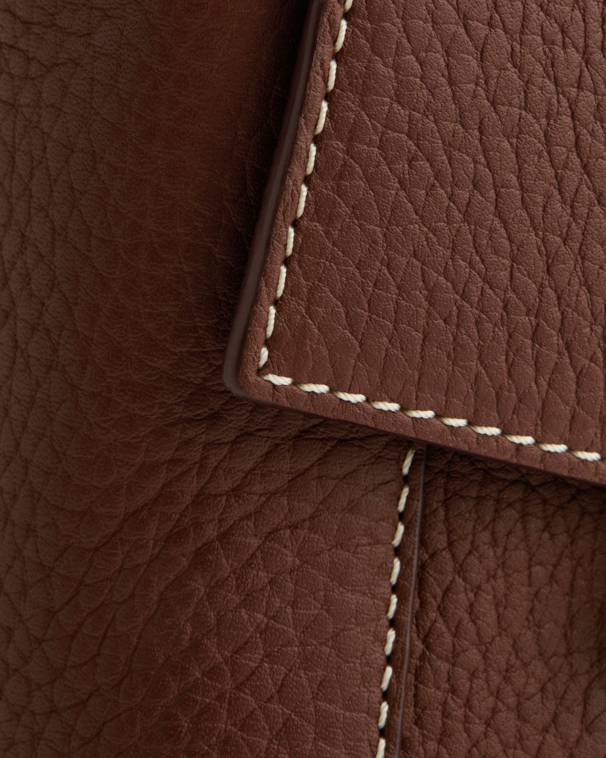 Close-up of chocolate leather bag flap with vanilla contrast stitching