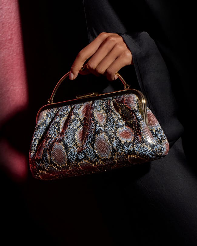 A woman's hand holding a snake skin purse