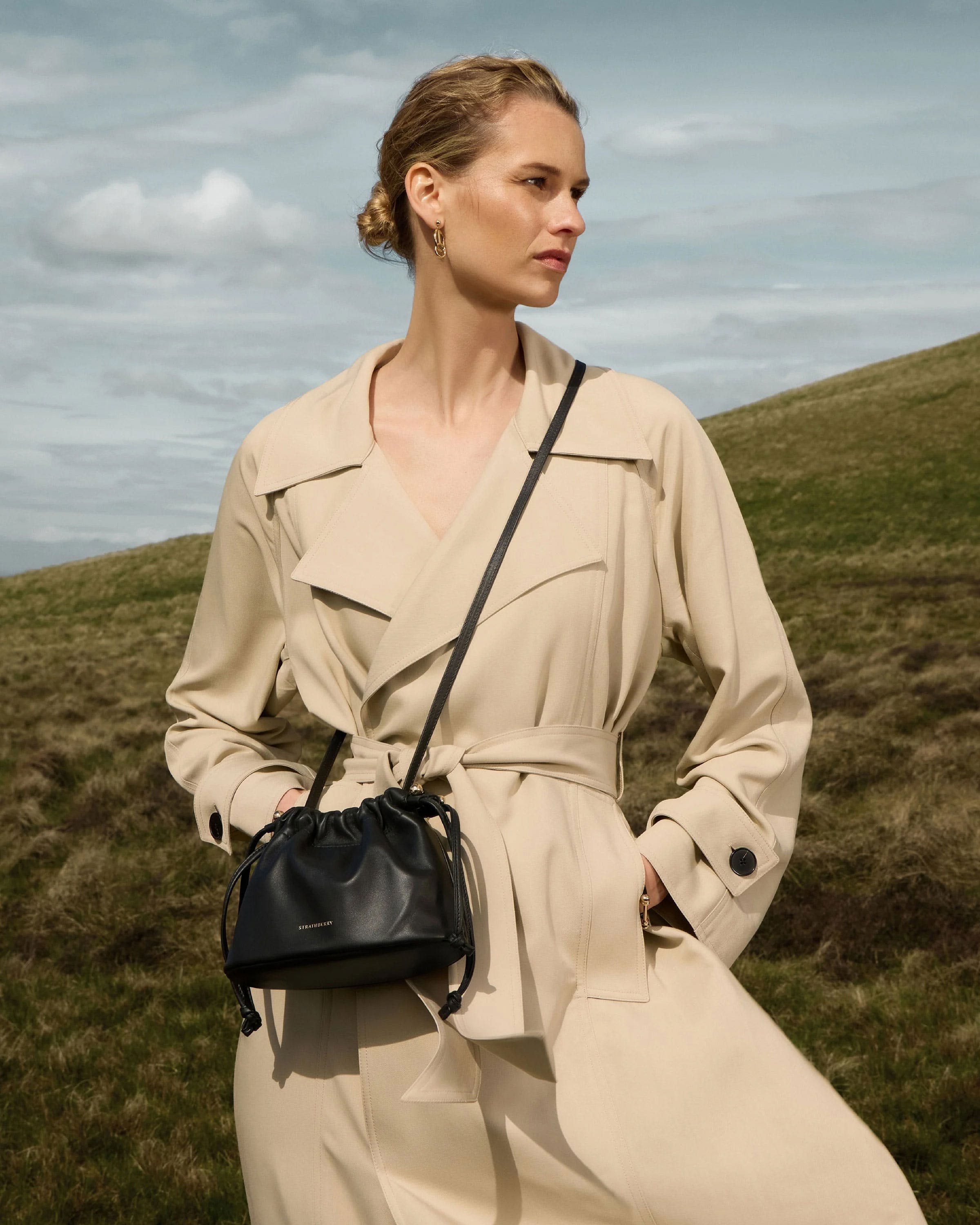 A woman in a trench coat holding a black purse