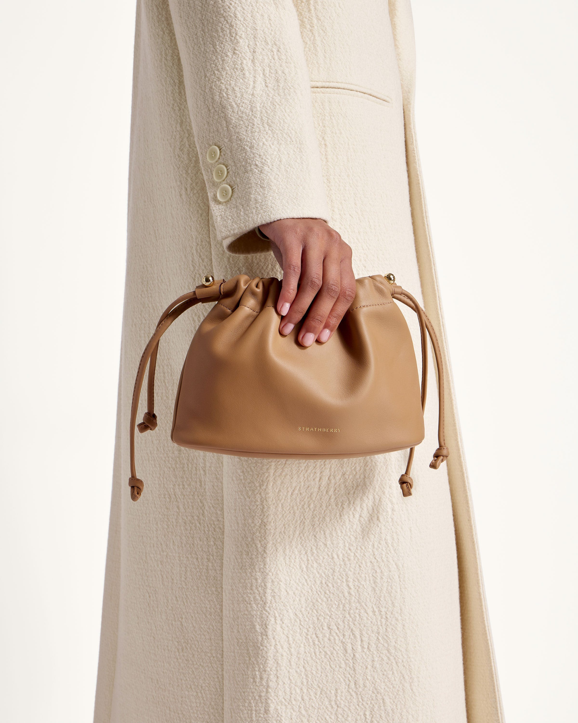 A woman in a white coat holding a tan purse