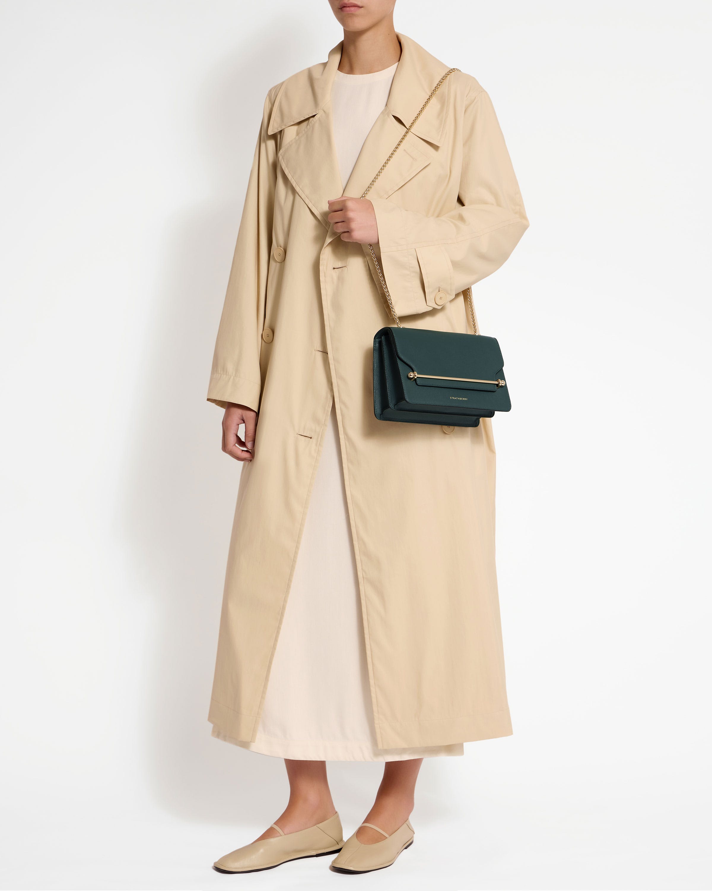 A woman wearing a trench coat and holding a green purse