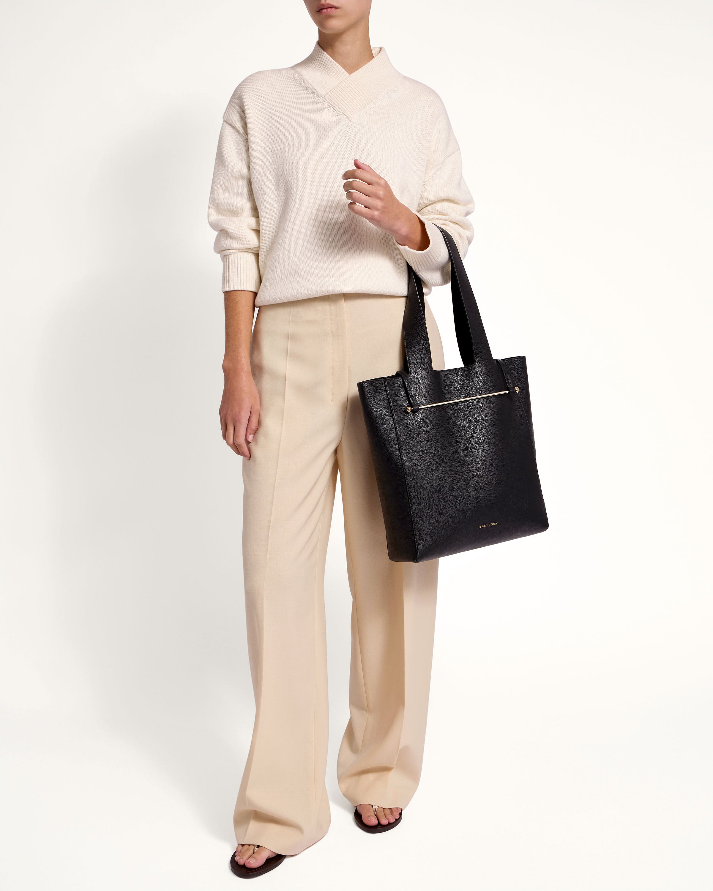 A woman in a white sweater and beige pants holding a black bag