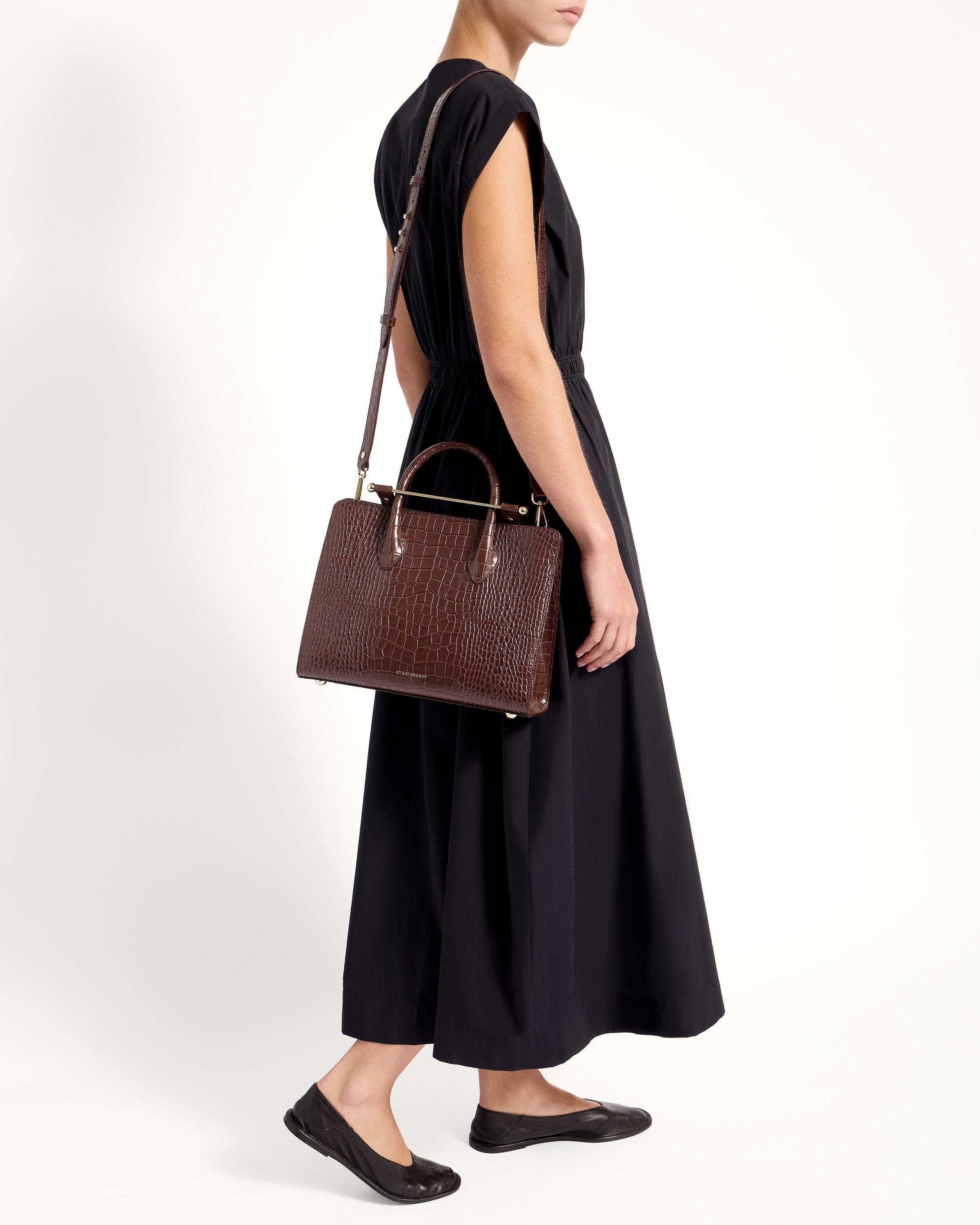 A woman in a black dress carrying a brown handbag