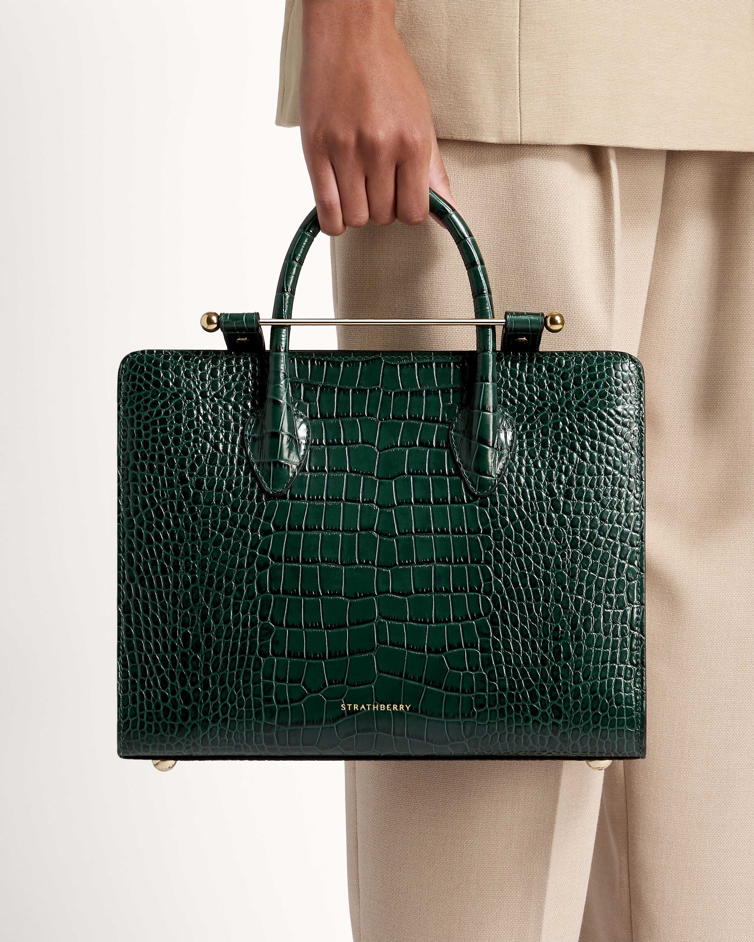 A person holding a green alligator skin briefcase