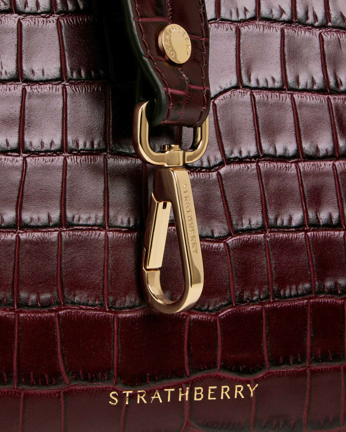 Burgundy croc midi tote close-up showing gold clasp and Strathberry logo.