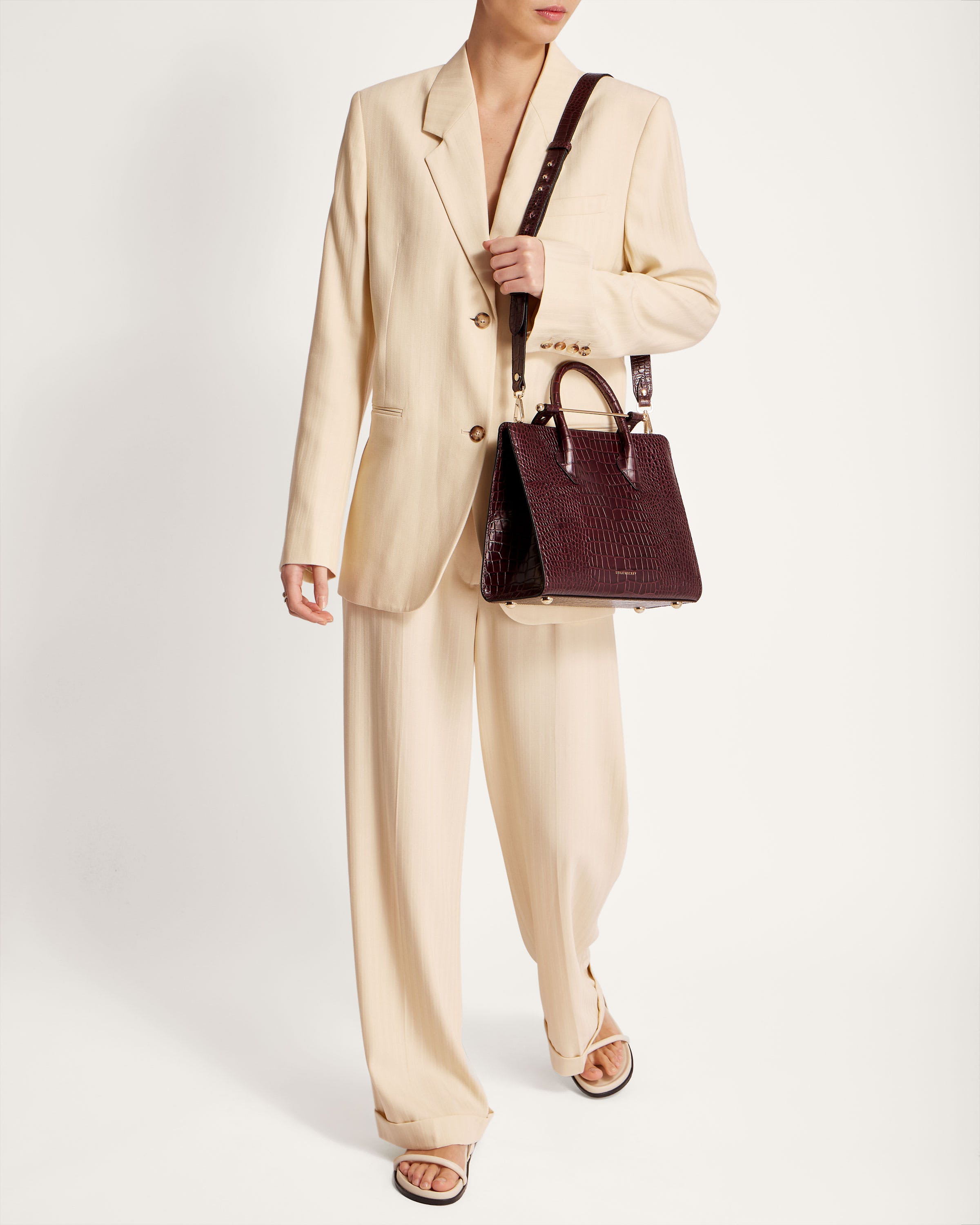 A woman in a white suit holding a brown purse