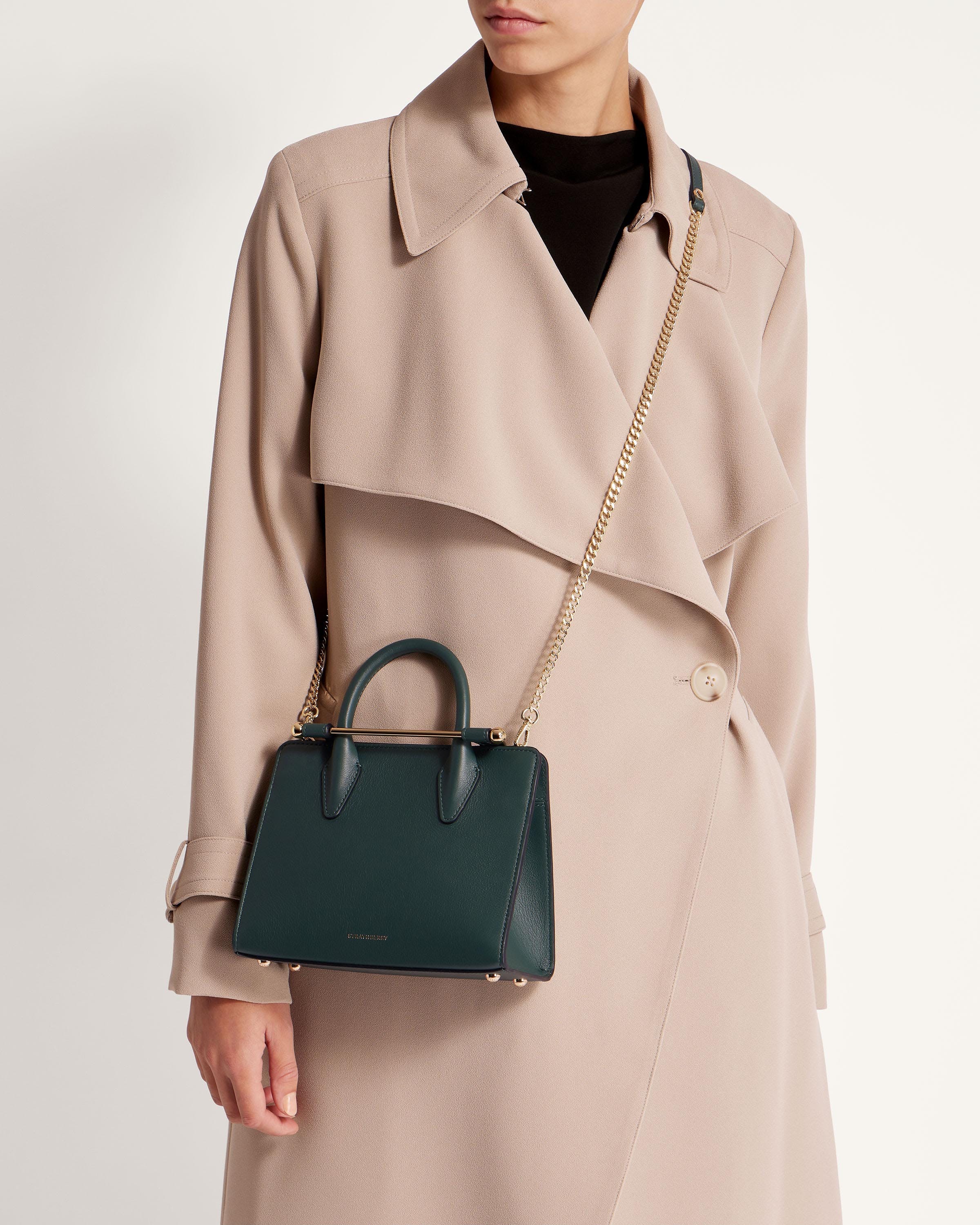 A woman in a trench coat holding a green handbag