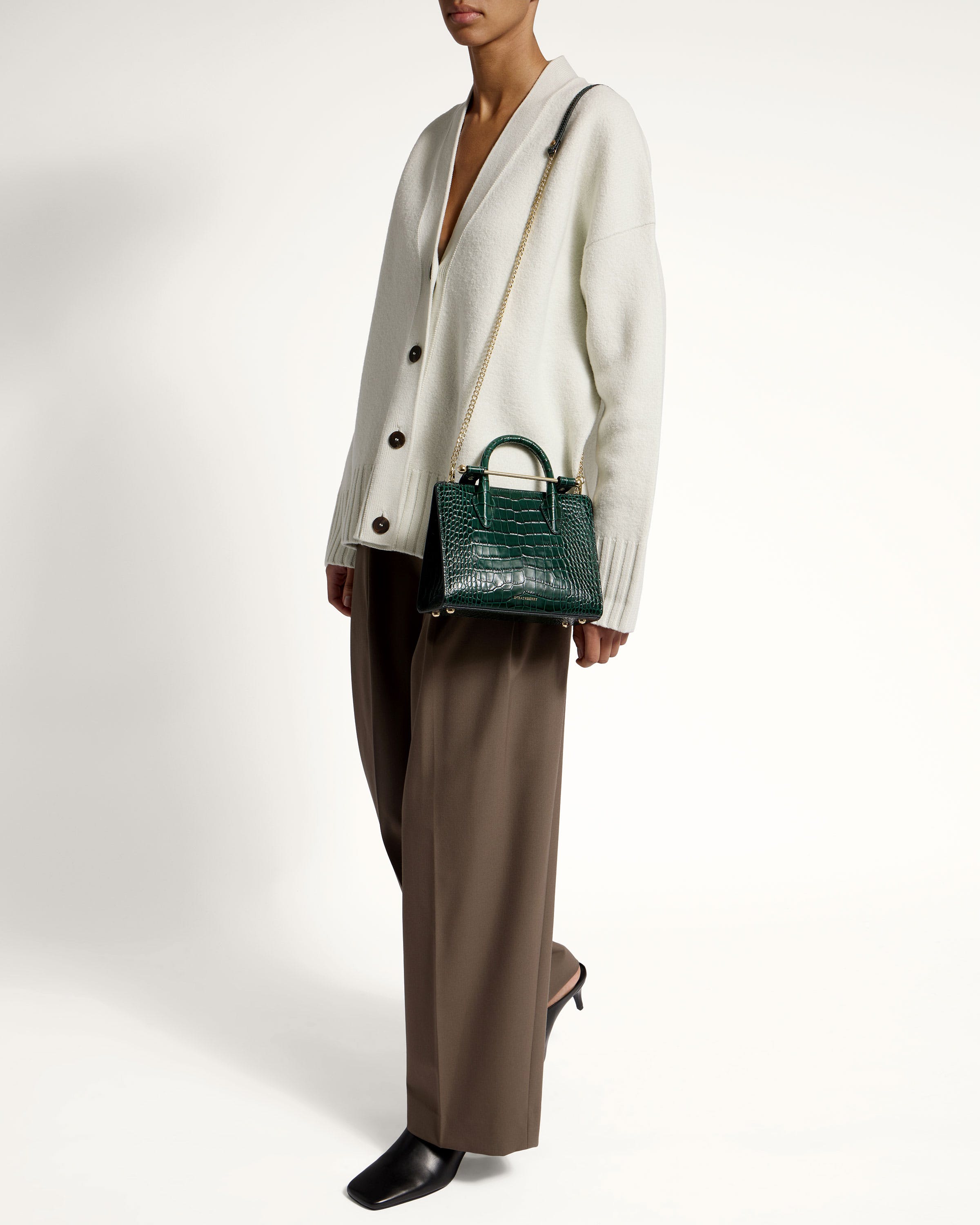 A woman in a white sweater and brown pants holding a green handbag