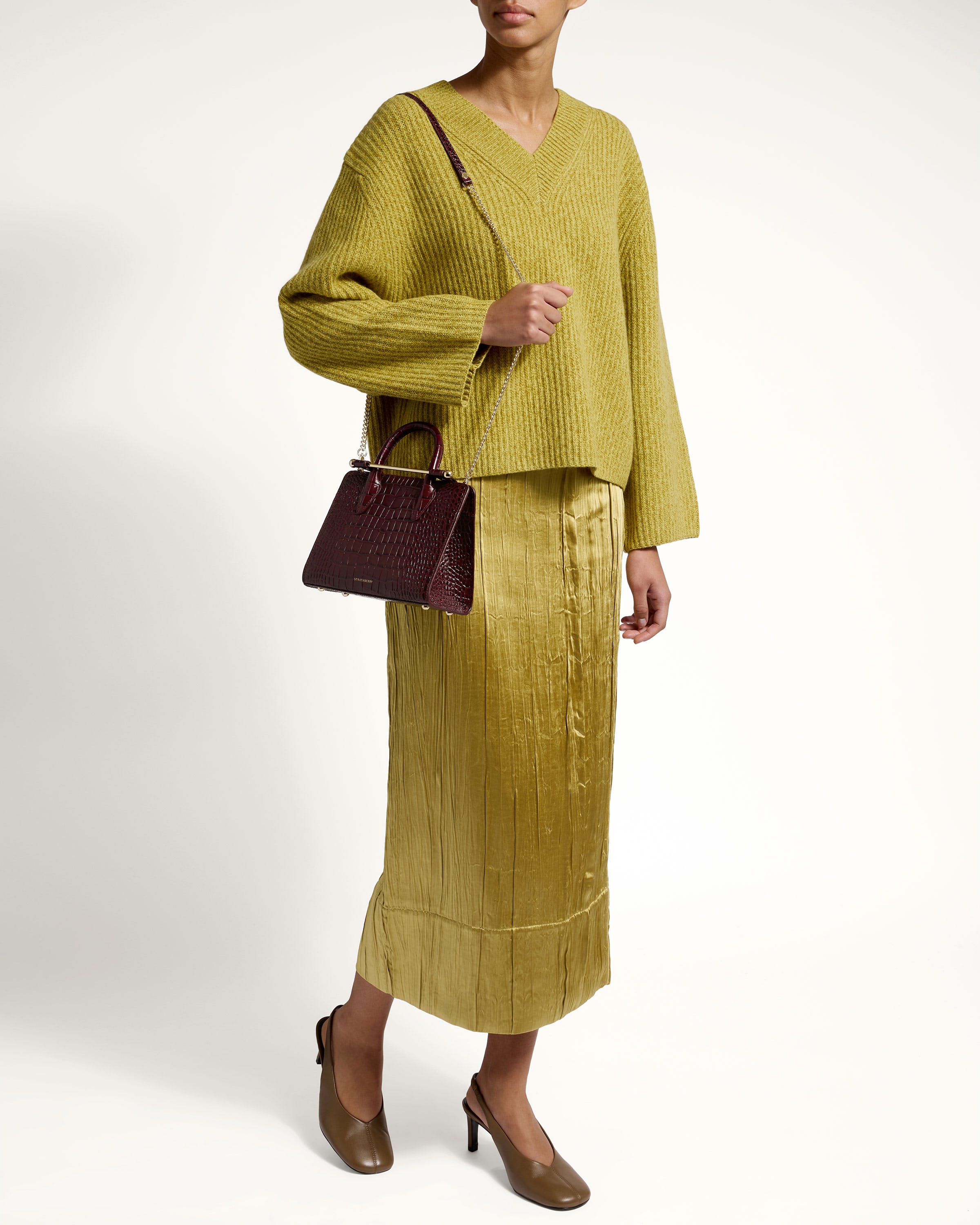 A woman in a yellow sweater and skirt holding a brown purse