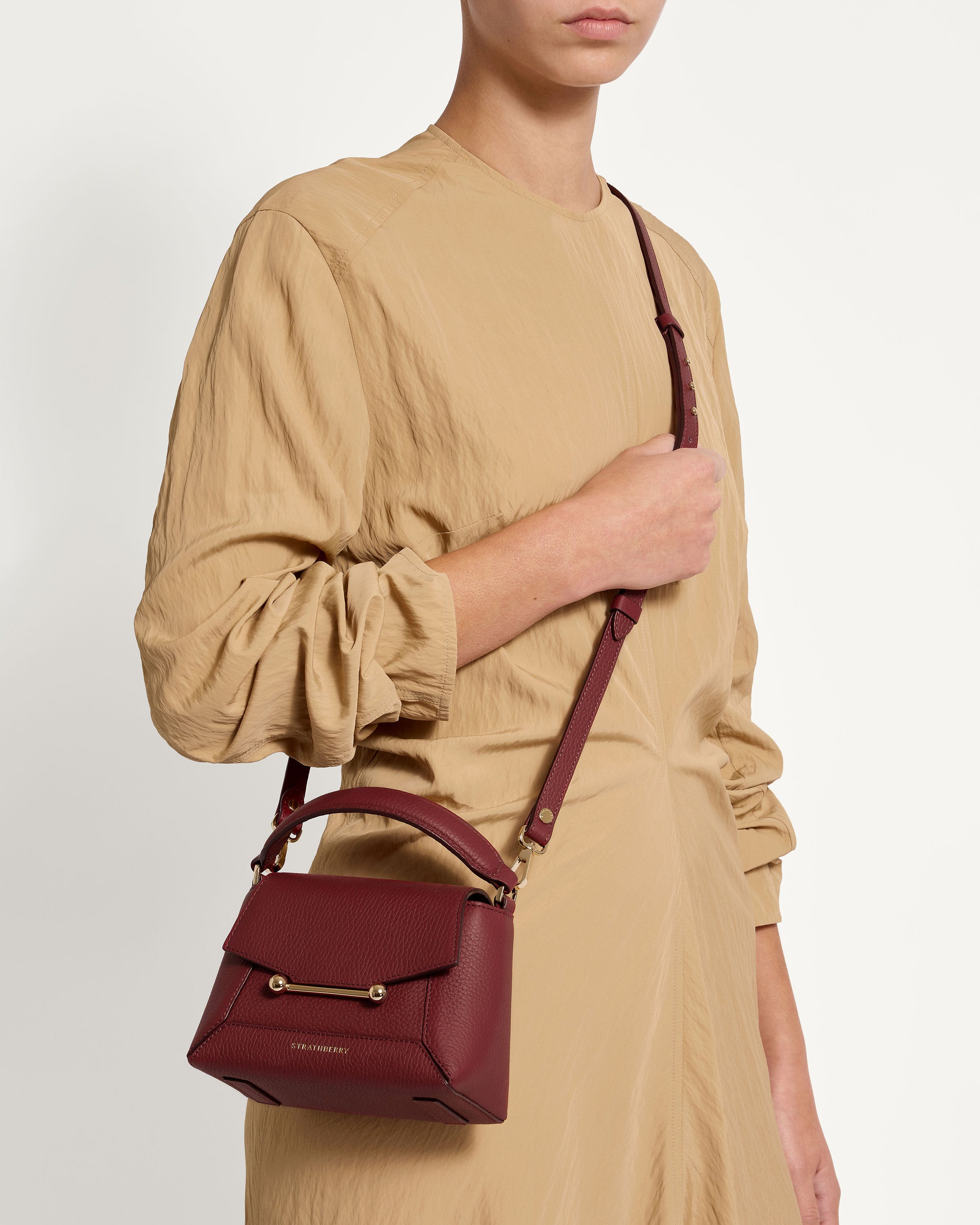 A woman in a tan dress holding a red handbag