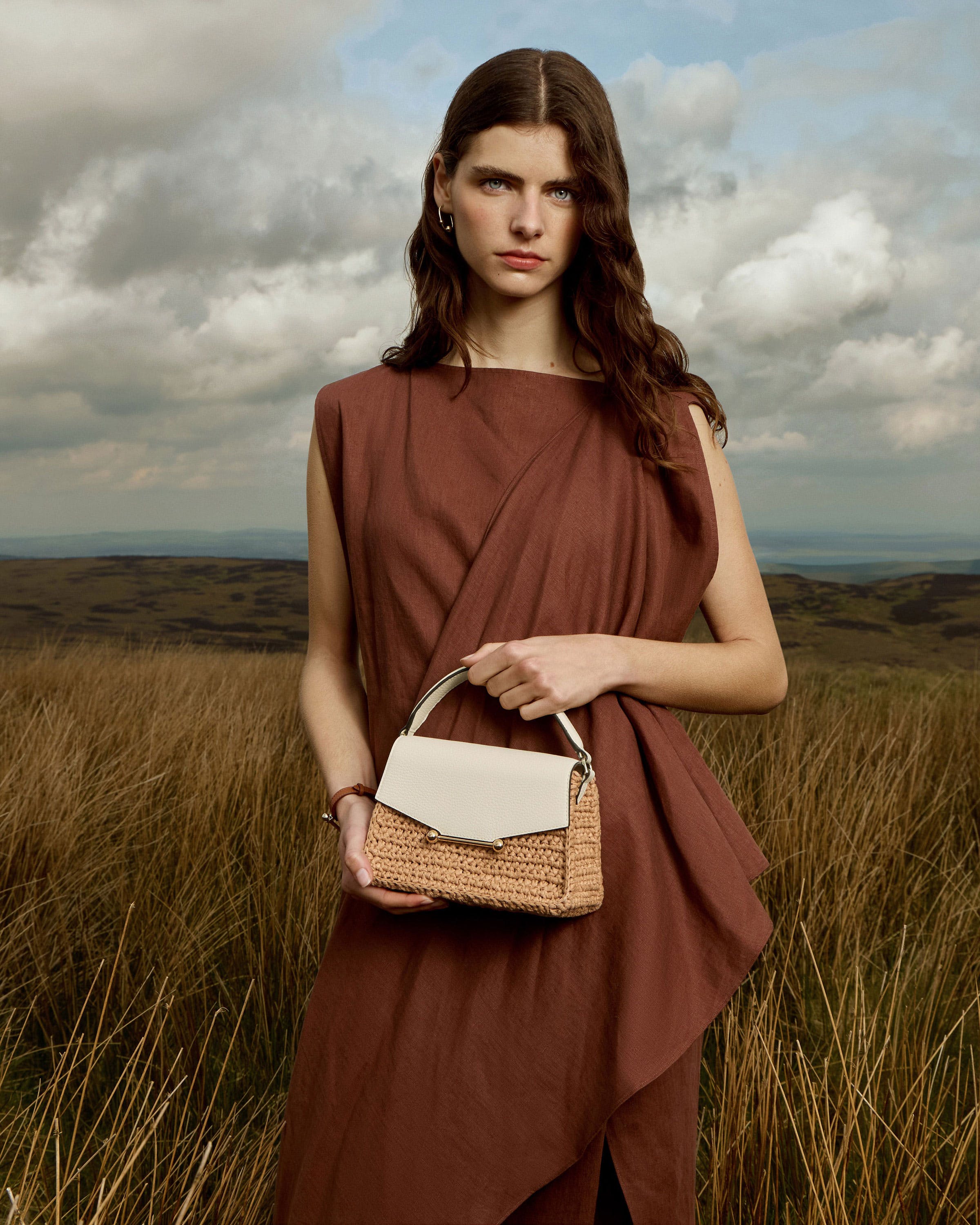 A woman standing in a field holding a purse