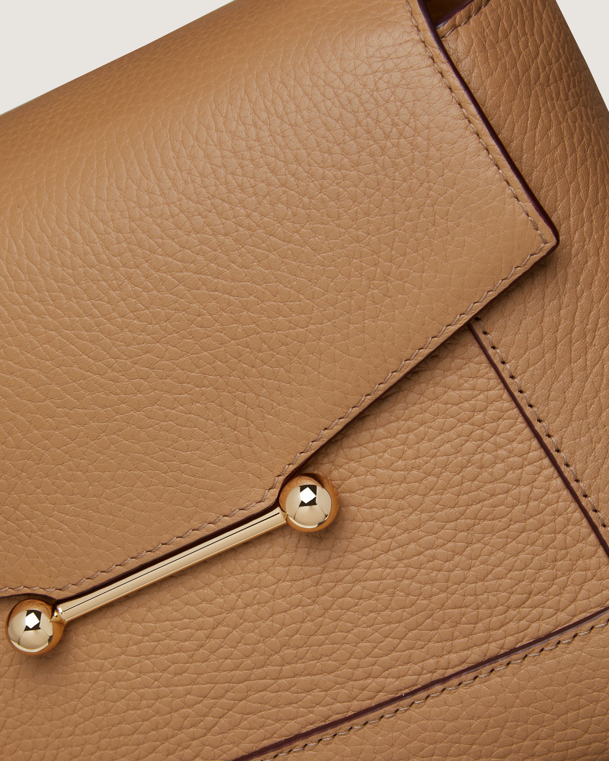 A tan leather purse with a gold metal handle