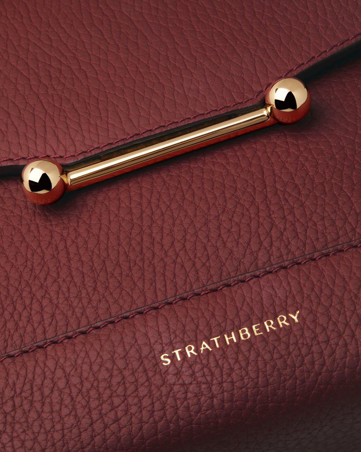 Close up of oxblood Strathberry Mosaic bag showing pebbled leather and gold bar.
