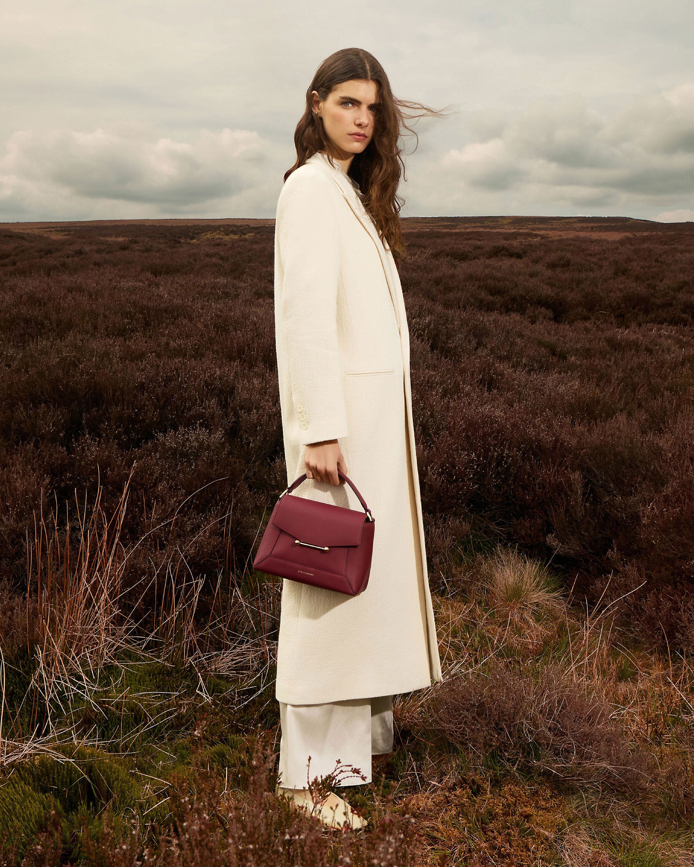 A woman standing in a field holding a red purse