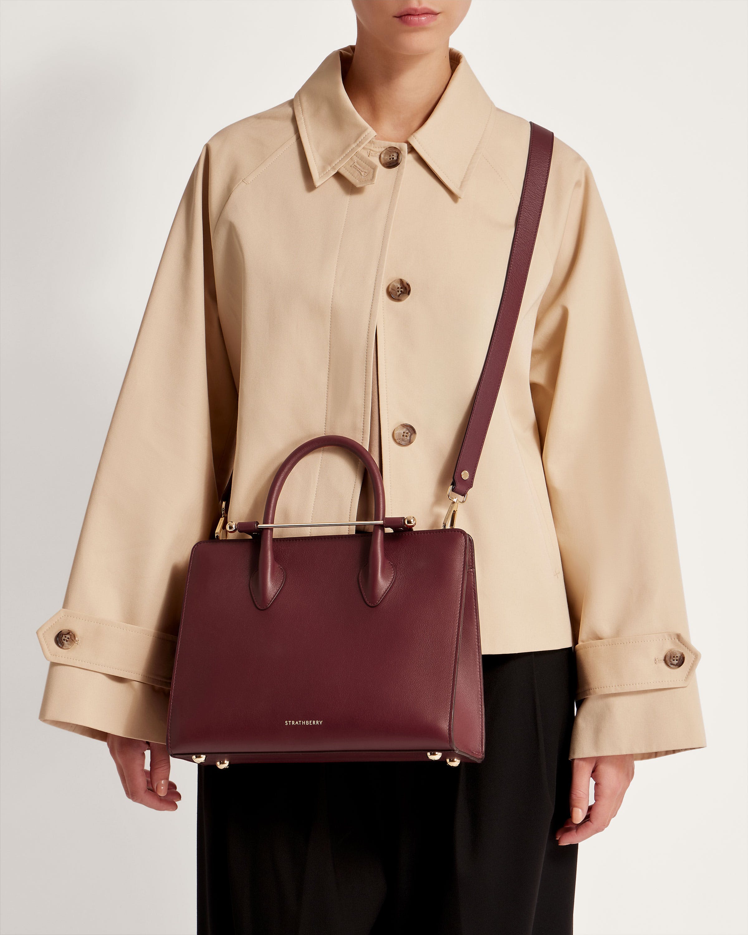 A woman in a trench coat holding a burgundy handbag