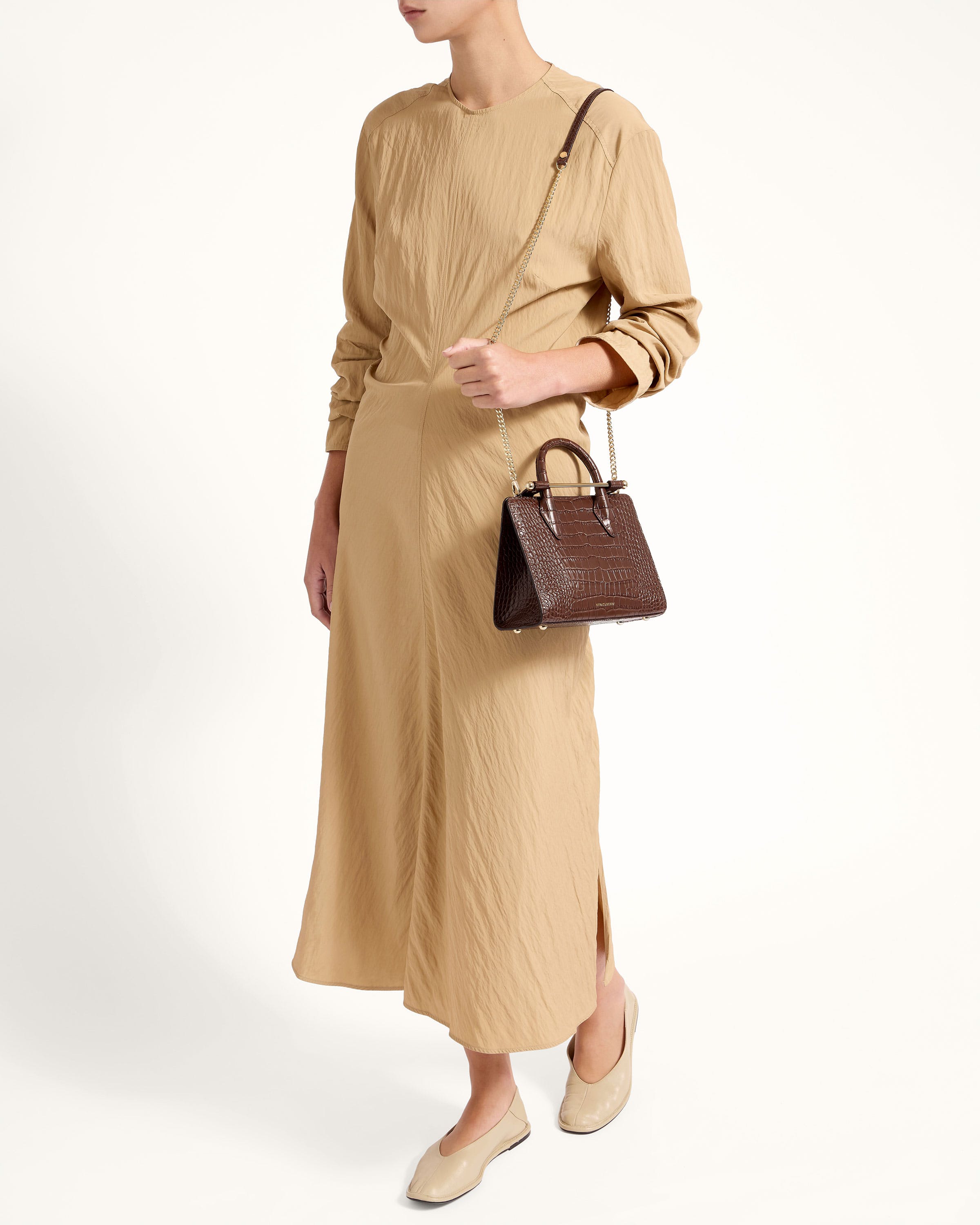 A woman in a tan dress holding a brown handbag