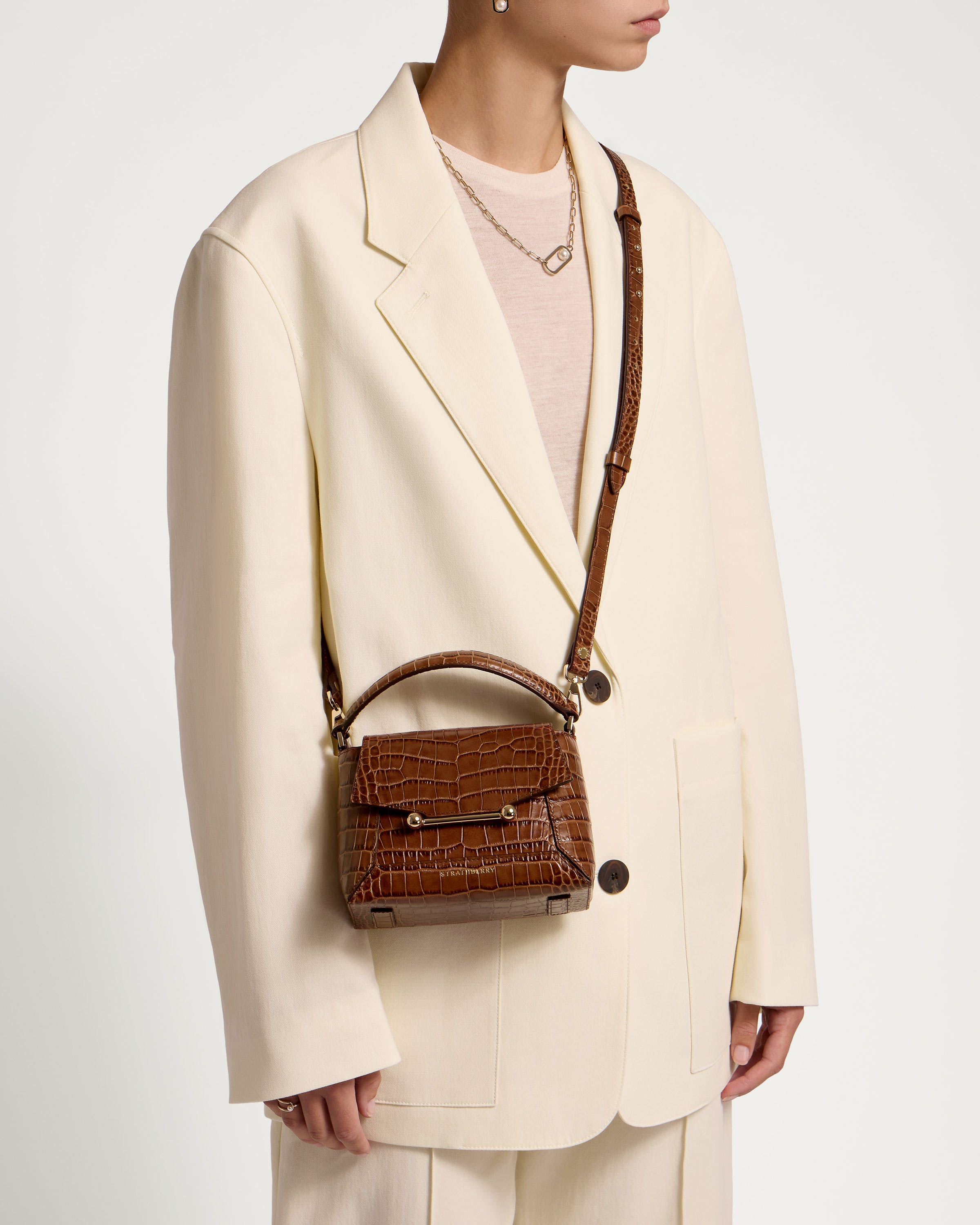 A woman wearing a white suit and a brown purse