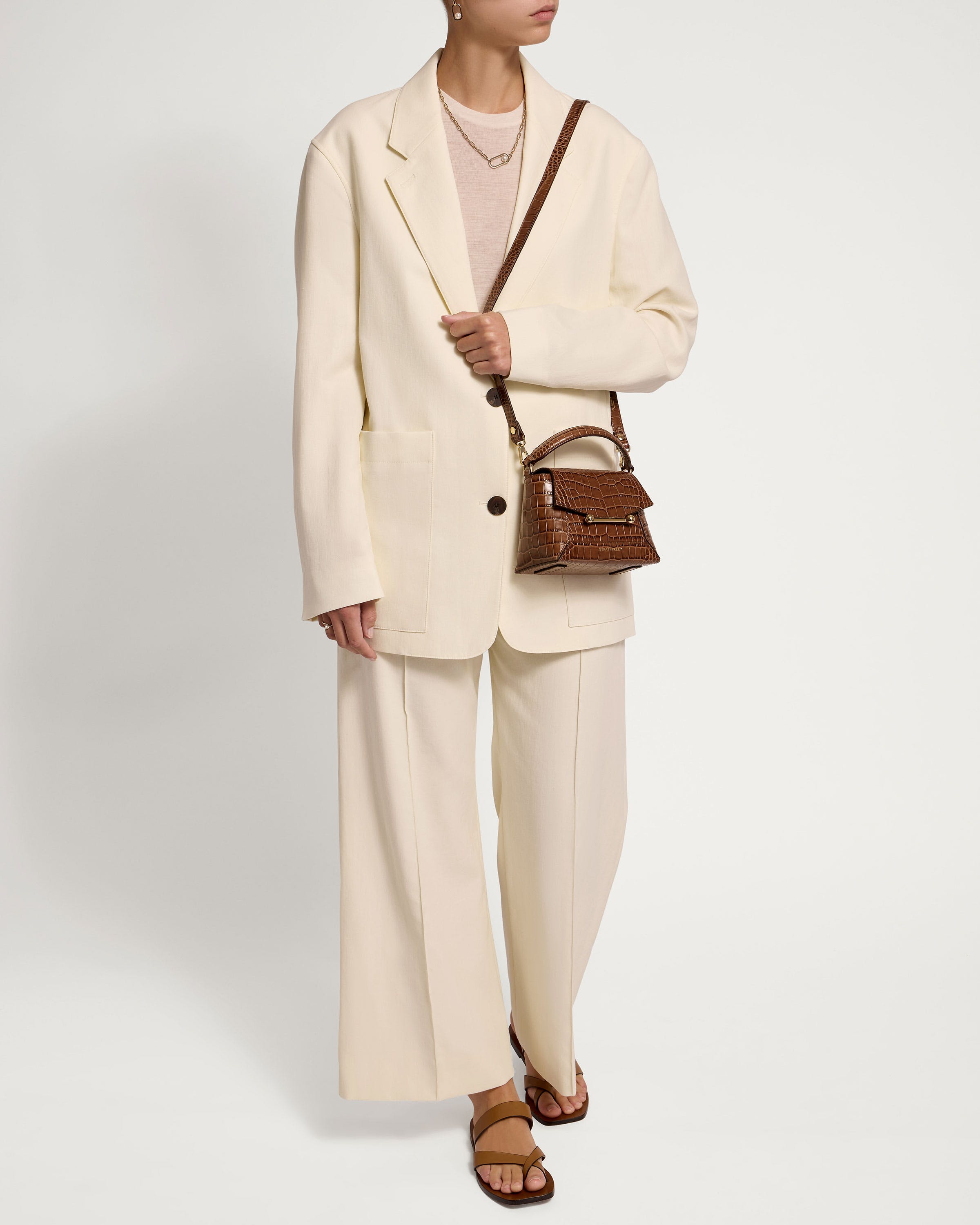 A woman in a white suit holding a brown purse