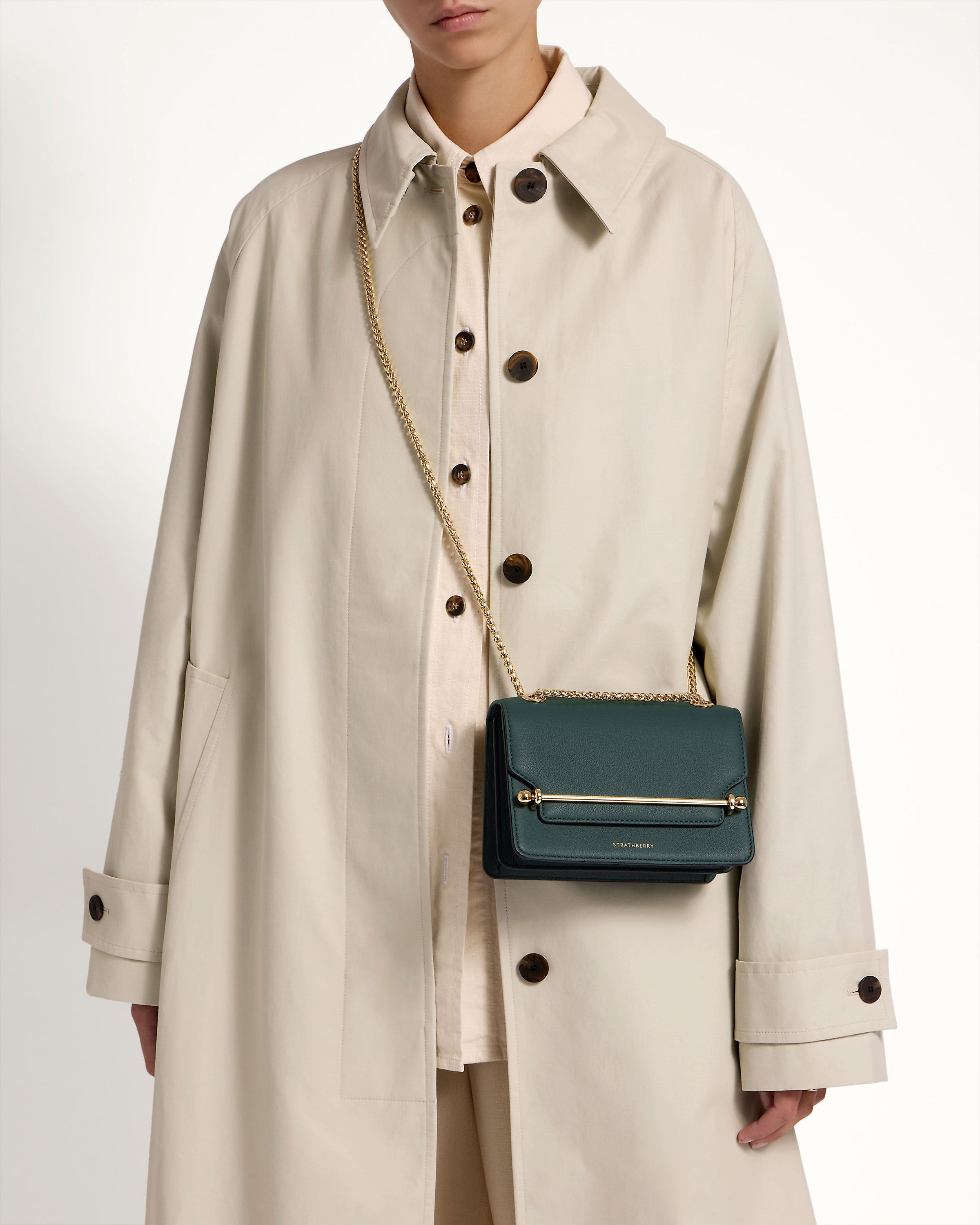 A woman in a trench coat holding a green purse