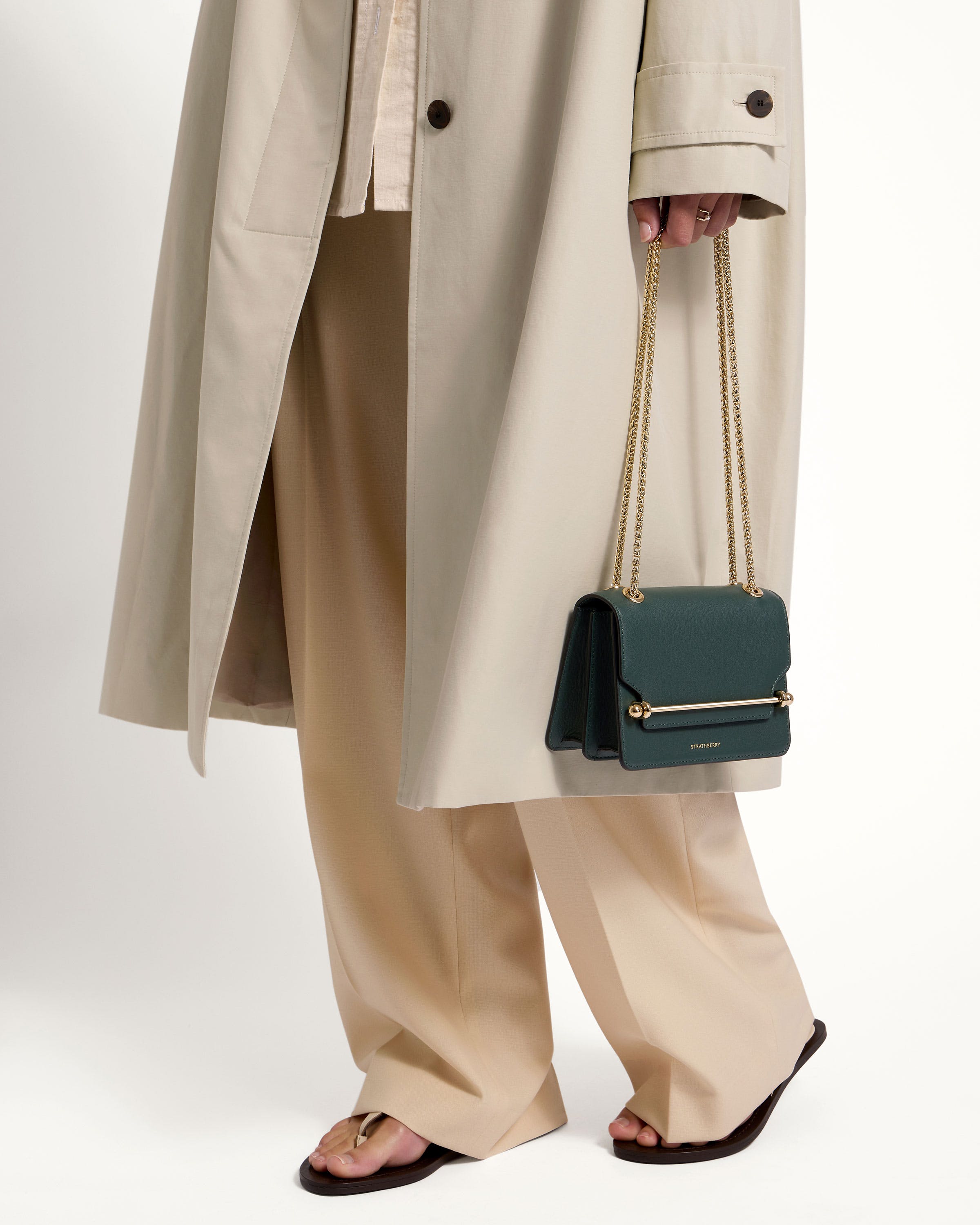 A woman in a trench coat holding a green purse