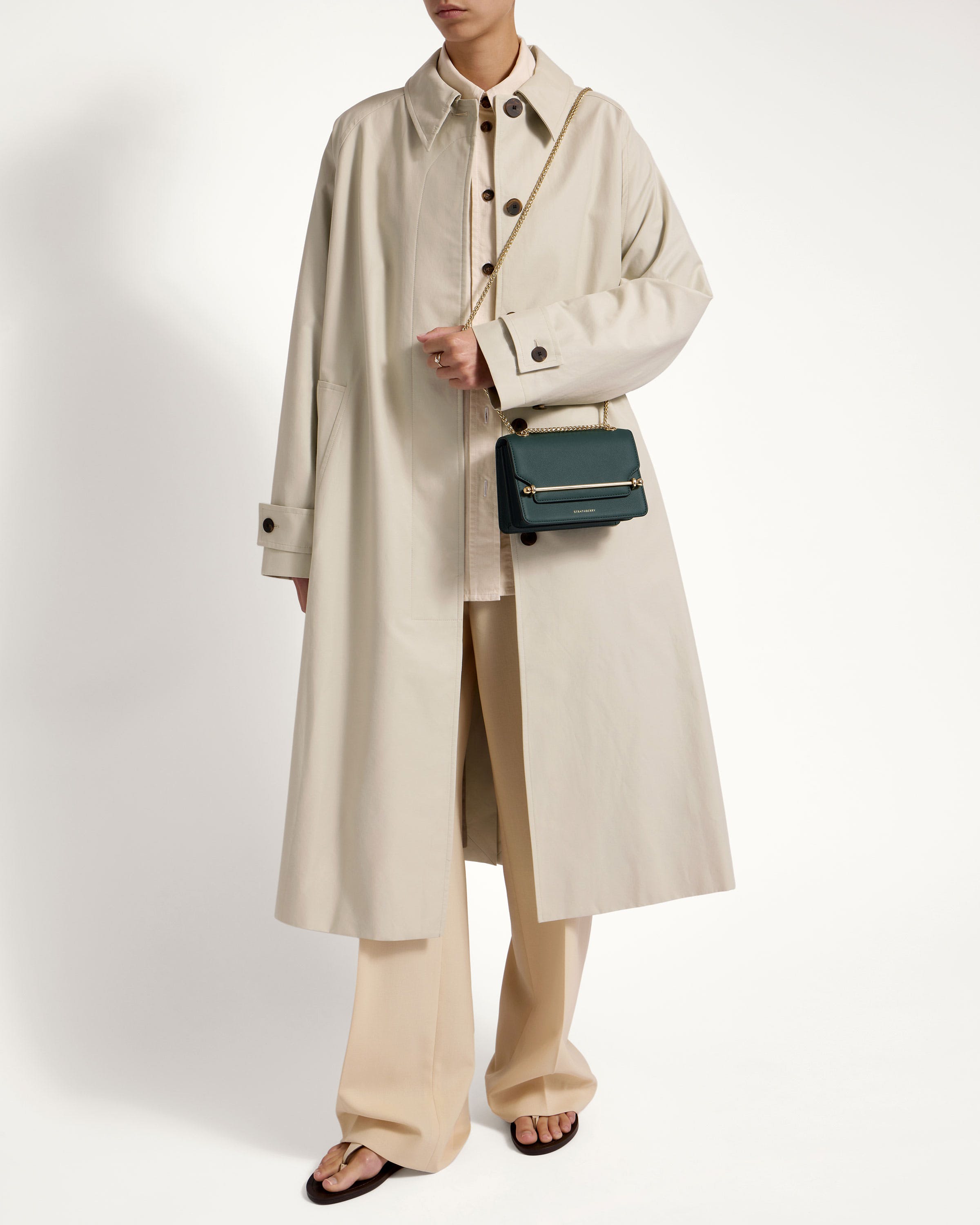 A man in a trench coat and pants holding a handbag